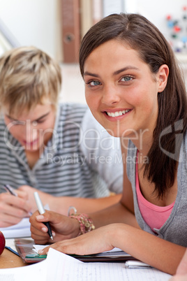Smiling teen girl studying in the library with her friends