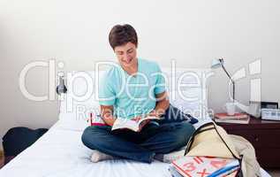 Smiling teenager reading a book in his bedroom