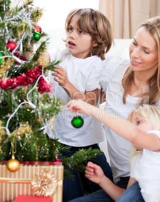 Smiling Mother and her children decorating a Christmas tree