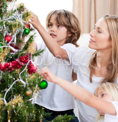 Children hanging Christmas decorations with their mother