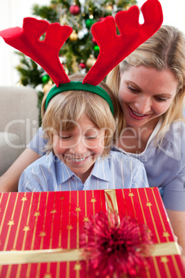 Smiling mother and her son opening Christmas present