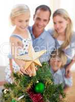 Father lifting his daughter to put the Christmas star on top of