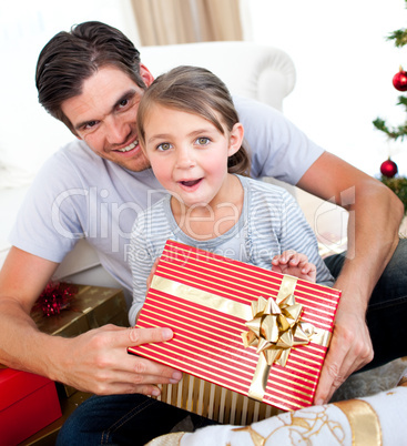 Surprised little girl opening a Christmas present with her fathe