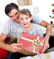 Surprised little girl opening a Christmas present with her fathe