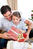 Surprised little girl holding a Christmas present with her fathe