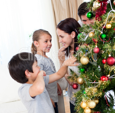 Smiling family decorating a Christmas tree with boubles