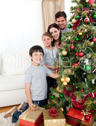 Happy family decorating a Christmas tree with boubles and presen