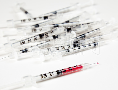 Pile of used syringes with a single one with fluid