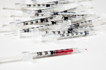 Pile of used syringes with a single filled one