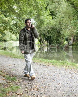 man on a mobile phone walking beside a canal or river