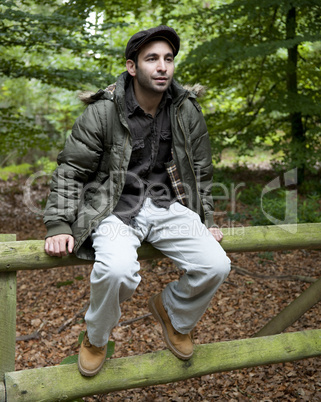 Man sitting on a fence in woodland.