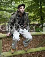 Man sitting on a fence in woodland.