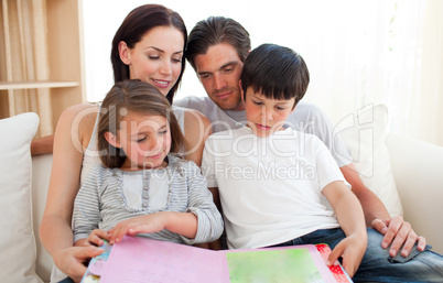Parents and their children reading a book on the sofa