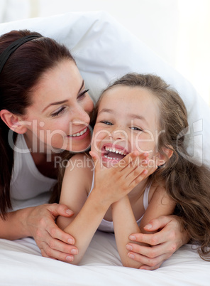 Little girl and her mother having fun on bed