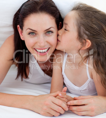 Little girl kissing her mother lying on bed
