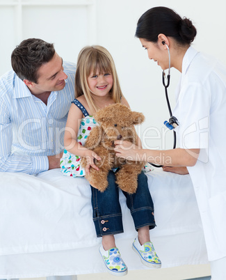 Female doctor and happy little girl examing a teddy bear