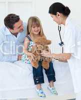 Female doctor and happy little girl examing a teddy bear