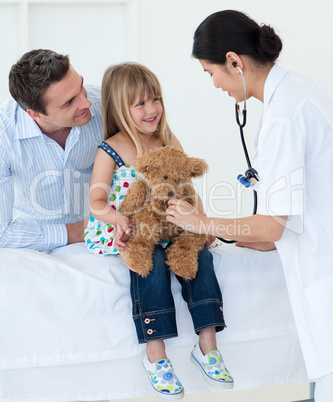 A doctor examining smiling child and playing with a teddy bear
