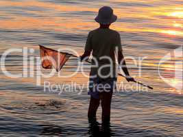 Kind mit Fischernetz vor Sonnenuntergang am Wasser