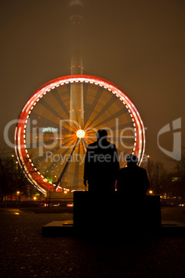 Marx und Engels Statuen am Alexanderplatz in Berlin mit Karussell im Hintergrund