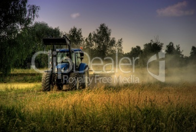 Trecker bei der Arbeit in der Abendsonne mit Staubwolke