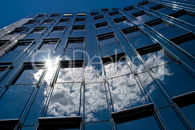 Wolken spiegeln sich in der Glasfassade eines modernen Bürohauses
