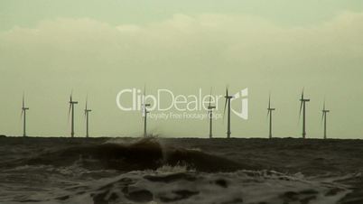 Low level shot of wind turbines at sea on a dark stormy day. slow motion