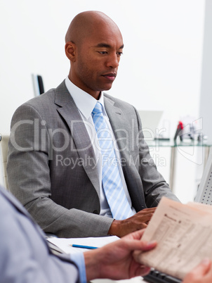 Businessman reading a newspaper with his colleague workig at a c