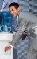 Attractive businessman filling cup from water cooler