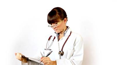 Female doctor in glasses recording something on notepad