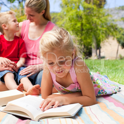 Concentrated blond girl reading while having a picnic with her f