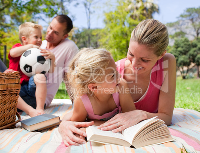 Mother and her daughter reading at a picnic with their family