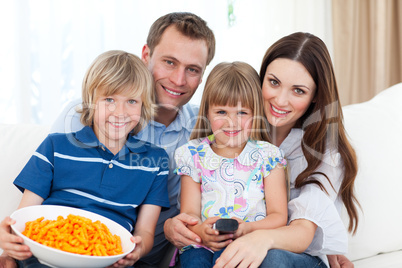 Portrait of a smiling family eating crisps while watching TV