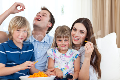 Young family eating crisps while watching TV