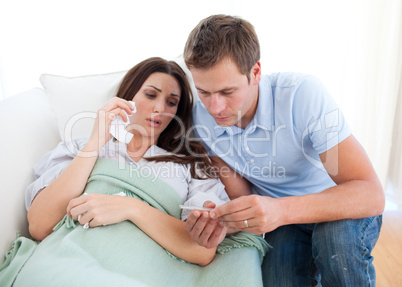 Husband taking his wife's temperature lying on the sofa