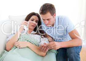 Husband taking his wife's temperature lying on the sofa