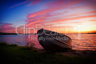 Image of fishing boat on shore of lake at sunset