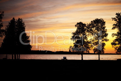 Elderly couple sitting on a bench by lake at sunset