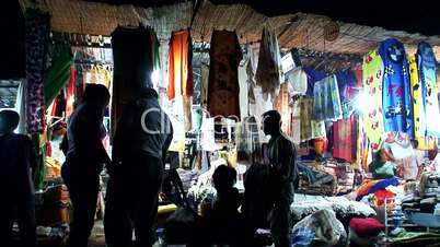 Customers browsing a street market bazaar in the evening.
