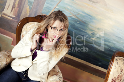 Sexy blond girl with glasses sitting on a luxury armchair