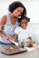 Attentive mother helping her girl cooking biscuits