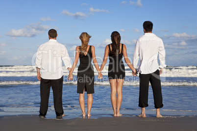 Four Young People, Two Couples, Holding Hands On A Beach