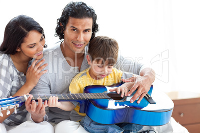 Cute little boy playing guitar with his parents