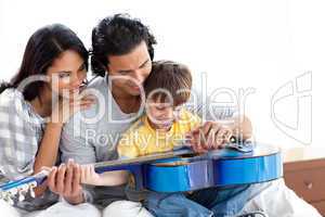 Happy little boy playing guitar with his parents