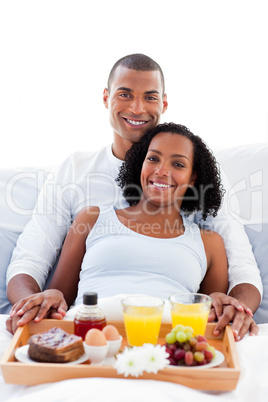 Afro-american couple having breakfast lying on their bed