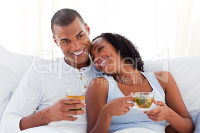 Happy ethnic couple drinking a cup of tea on their bed