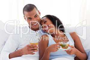 Happy ethnic couple drinking a cup of tea on their bed