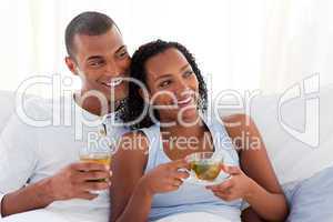 Jolly couple drinking a cup of tea on their bed