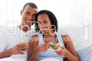 Smiling couple drinking a cup of tea on their bed