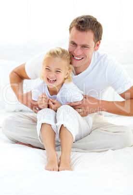 Attractive father playing with his little girl on a bed